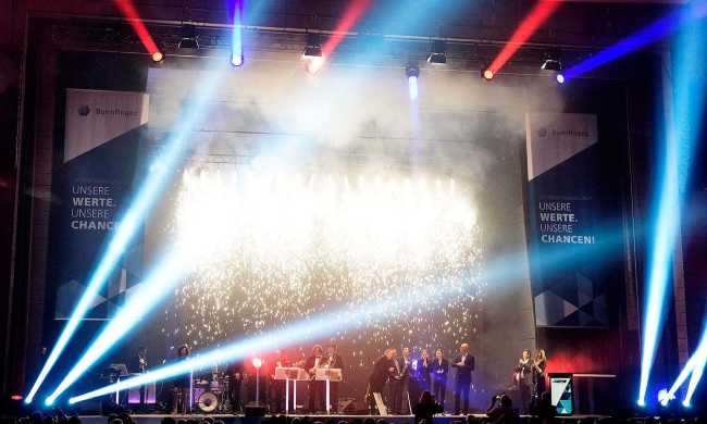 Stark beleuchtete Bühne mit schick angezogenen Gästen